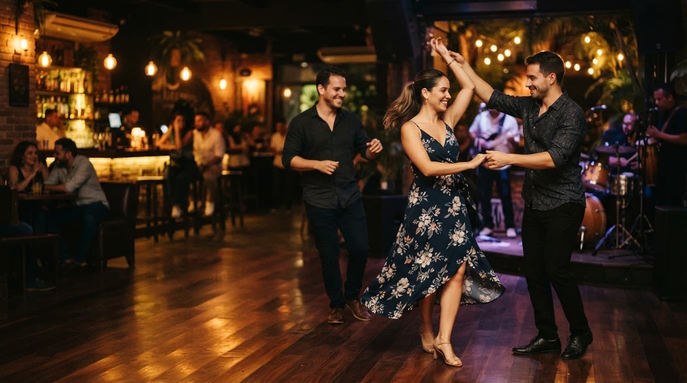 Three dancers perform salsa on a warmly lit club dance floor.