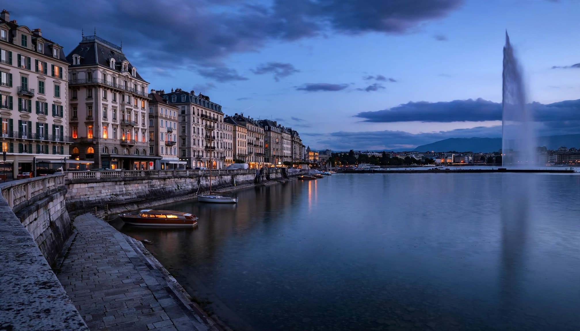 The Jet d'Eau rises beyond Geneva's quiet waterfront at blue hour.