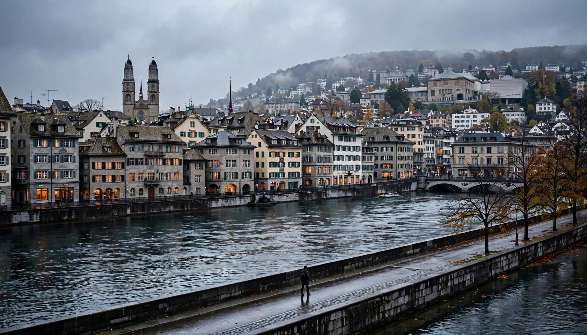 A lone walker follows the Limmat past Zurich's old town under gray skies.