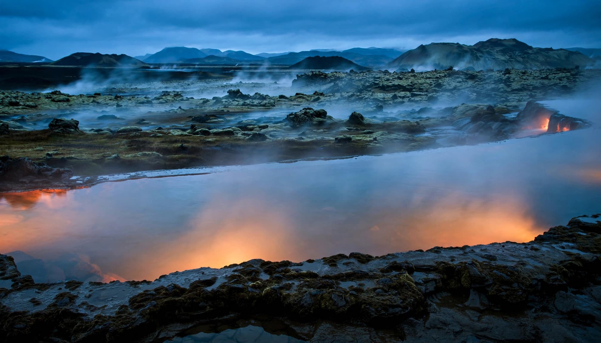 Steaming geothermal pool in a mossy lava field at blue hour.
