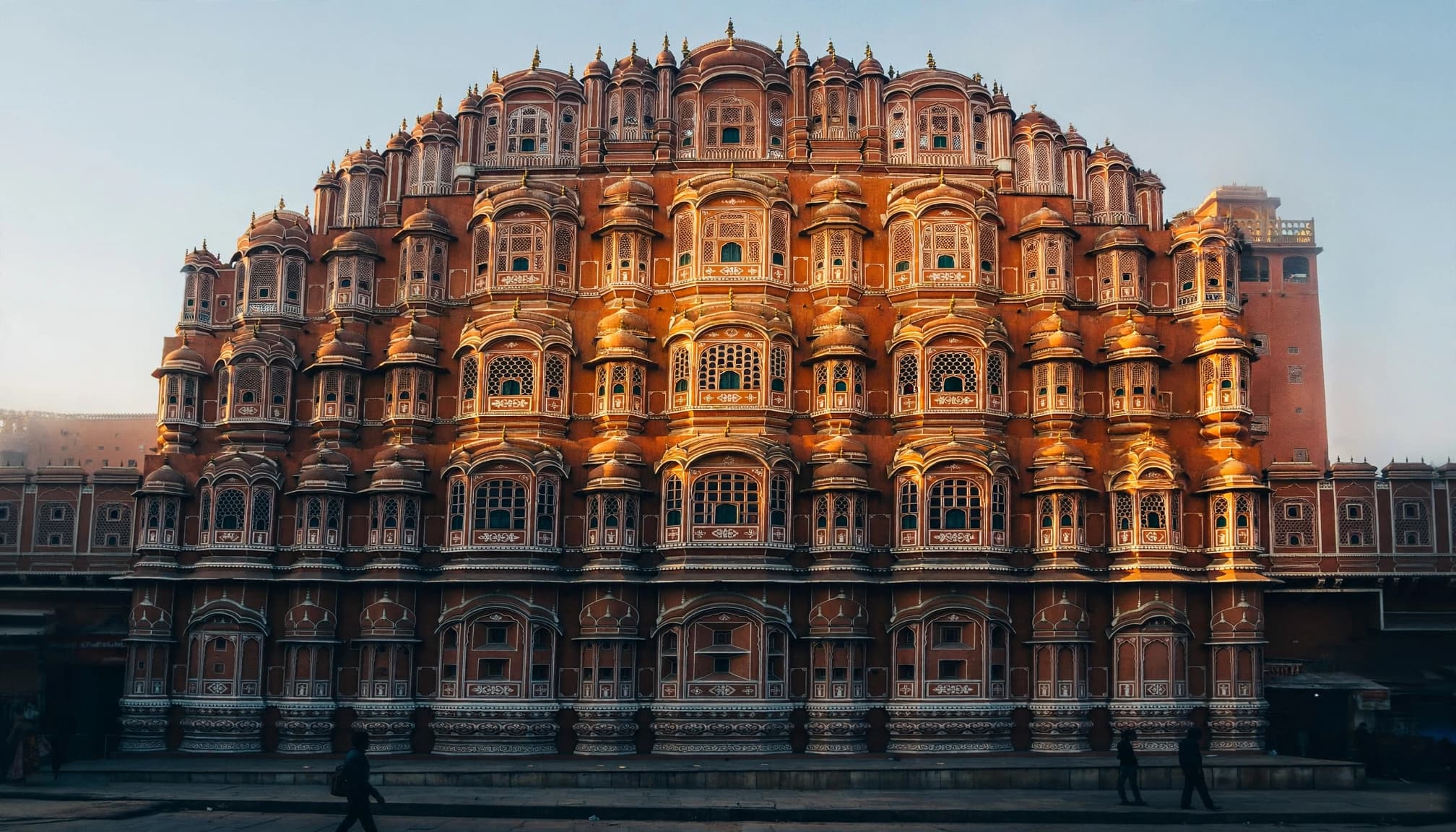 A photograph of the ornate pink sandstone facade of Jaipur's Hawa Mahal at sunrise.