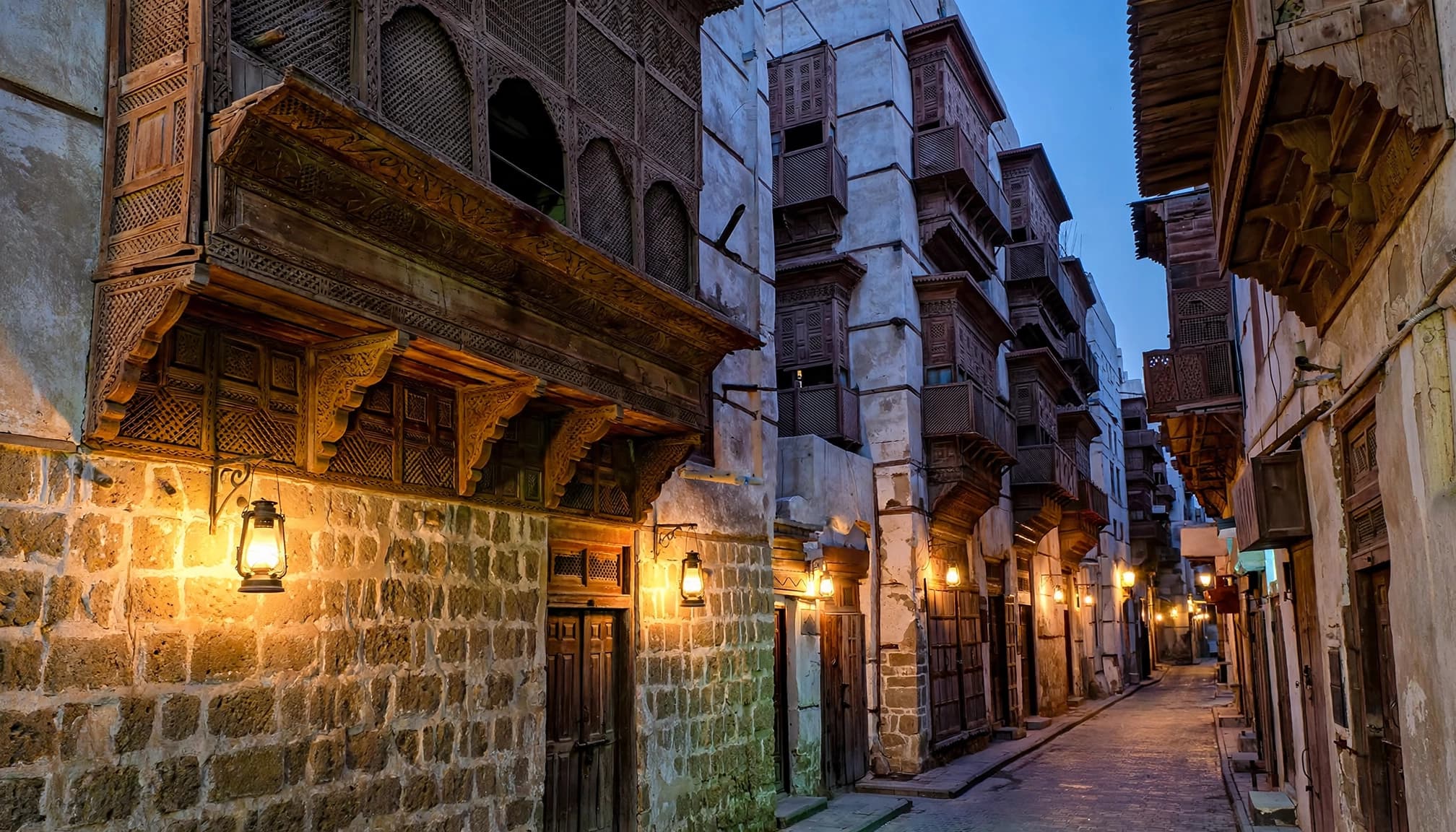 A narrow historic street in Jeddah with traditional coral-stone buildings and ornate wooden balconies.