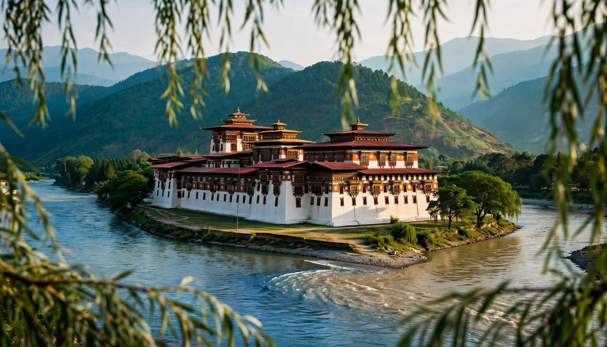 Punakha Dzong stands above a river, framed by willow branches and green hills.